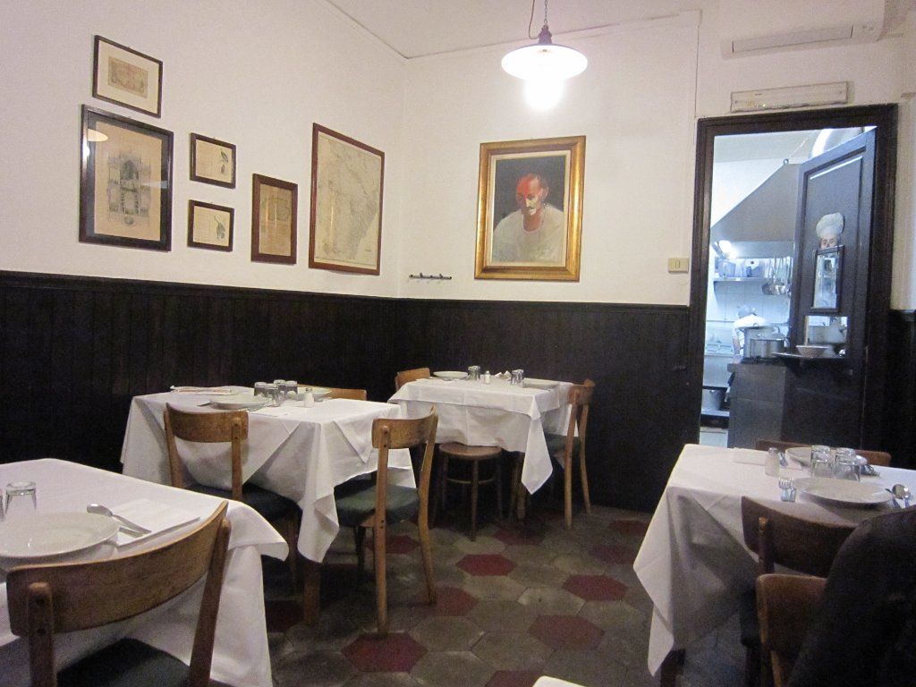 Una saletta con legno scuro a mezza parete, pavimento a esagonette e tavoli apparecchiati di bianco